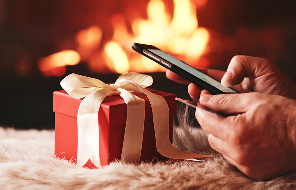 A person holding an award-winning, red gift box with a cell phone in front of a fireplace.